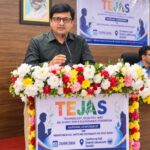 Sansar Green Managing Director Rajeev Singh speaking into a microphone behind a flower-decorated podium with TEJAS signage.